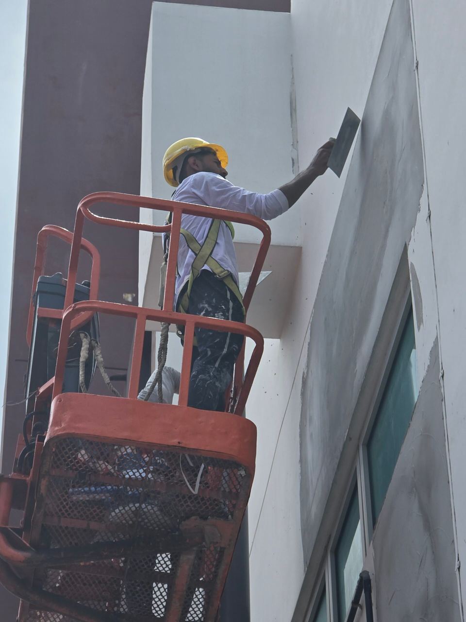 Eco Painting Service painter in a hard hat and full safety harness skimming a facade from a boom lift